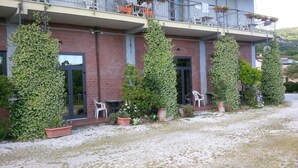 Ein Gebäude mit Ziegelaußenwand, großen Fenstern und einem Balkon mit orangefarbenen Stühlen. Kübelpflanzen und Kiesgrund sind ebenfalls vorhanden.