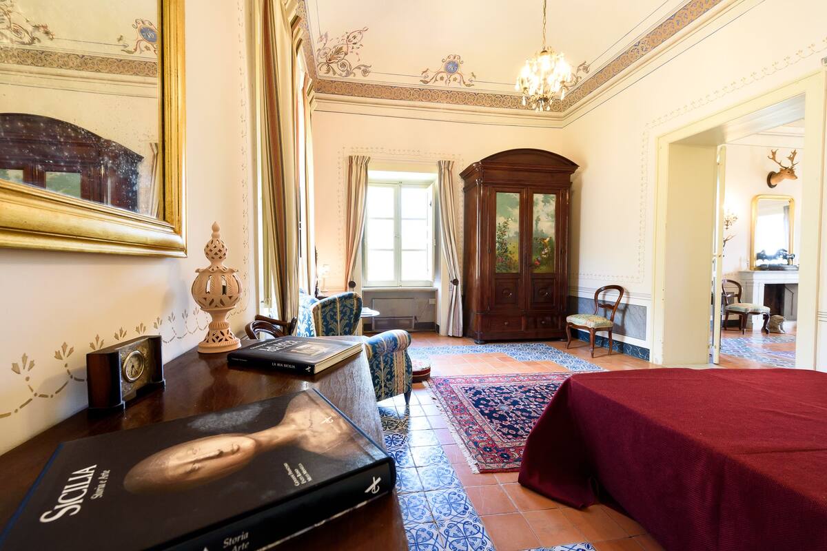 Una habitación con un espejo grande, un armario de madera, una colcha roja y una alfombra estampada.