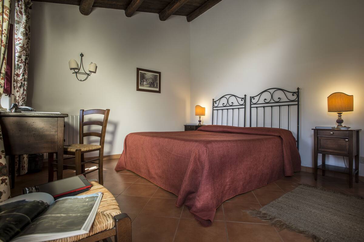 Un dormitorio con una cama, un escritorio, una silla, una lámpara y un cuadro en la pared.