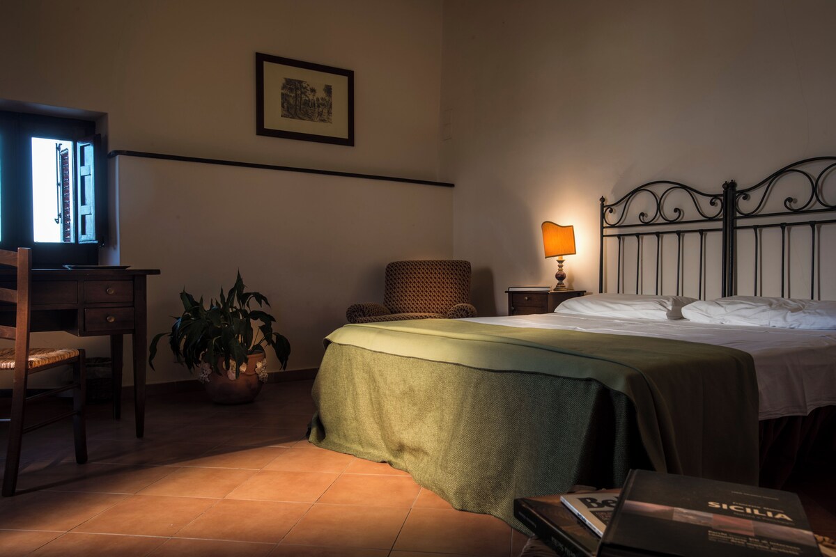 Un dormitorio con cama, escritorio, silla, lámpara y planta en maceta.