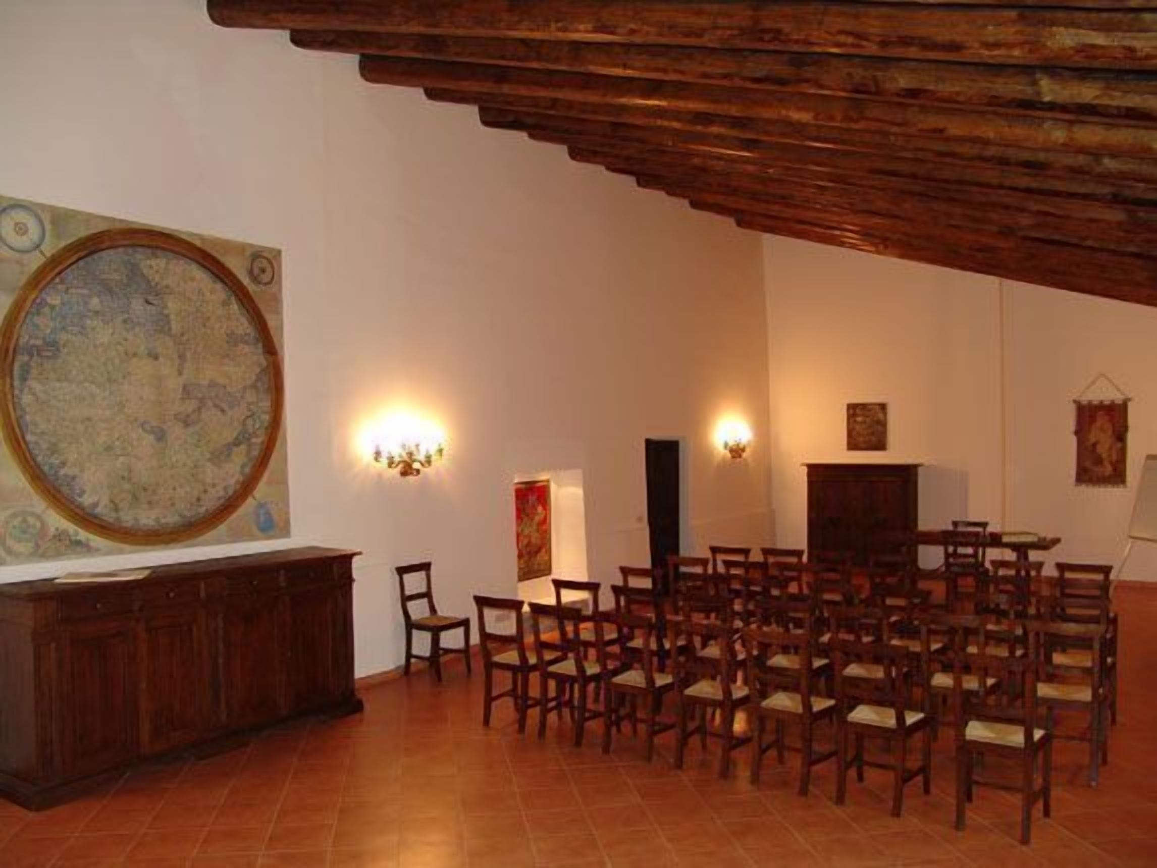 A spacious room with a high ceiling, a large map on the wall, and several wooden chairs arranged for seating.