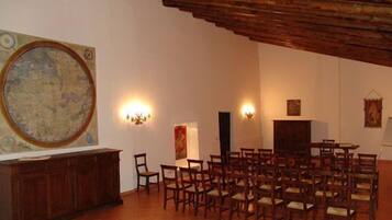 A spacious room with a high ceiling, a large map on the wall, and several wooden chairs arranged for seating.