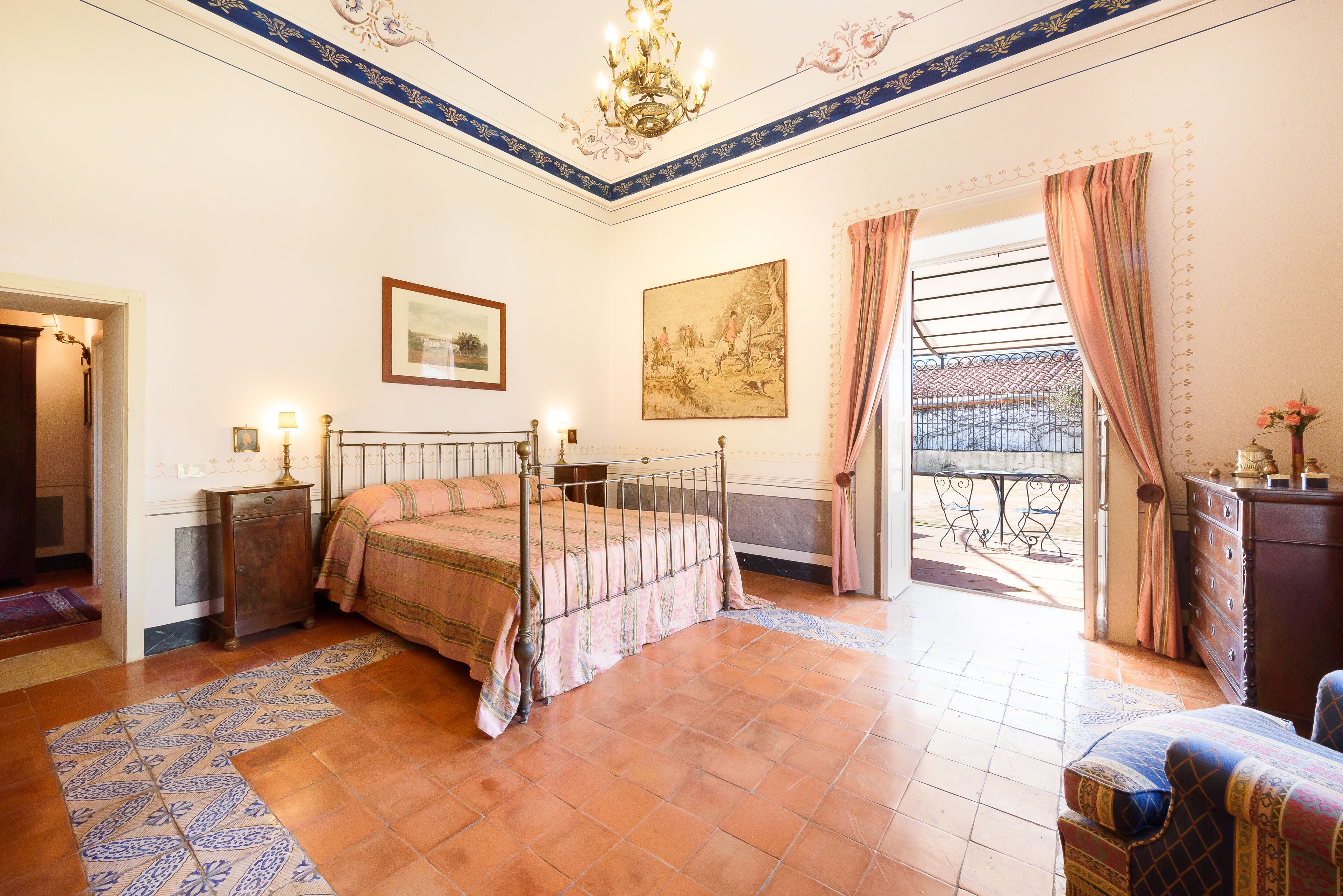 Ein Schlafzimmer mit Himmelbett, einer Kristallleuchter, einem Gemälde und Blick auf den Balkon.
