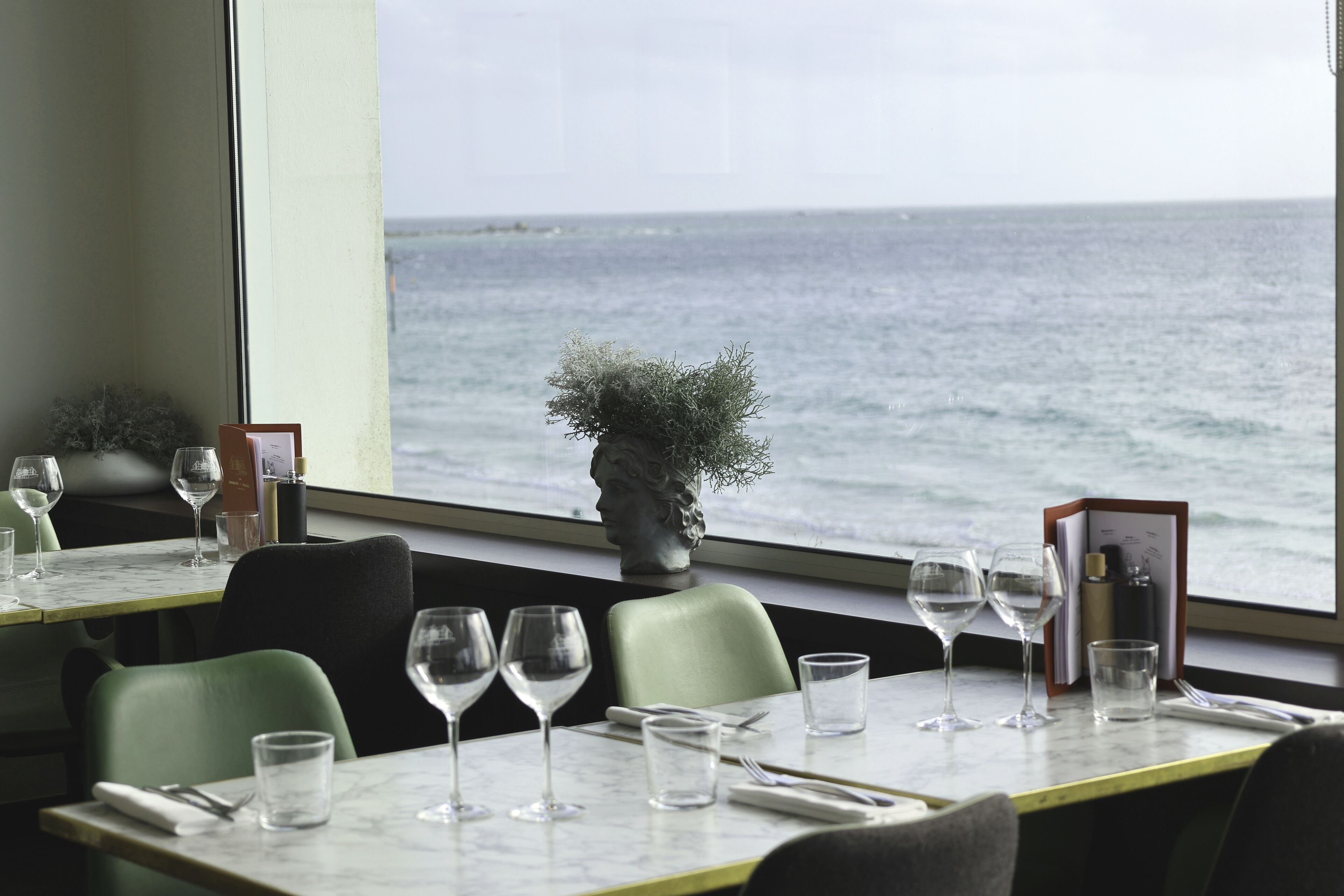 A dining table with wine glasses and a menu, set against a view of the sea.