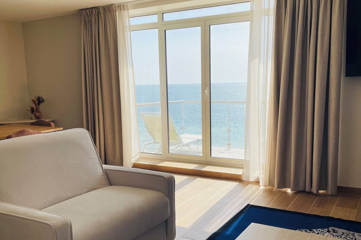 Una habitación de hotel con un ventanal grande, un sofá, una mesa de centro y un televisor.
