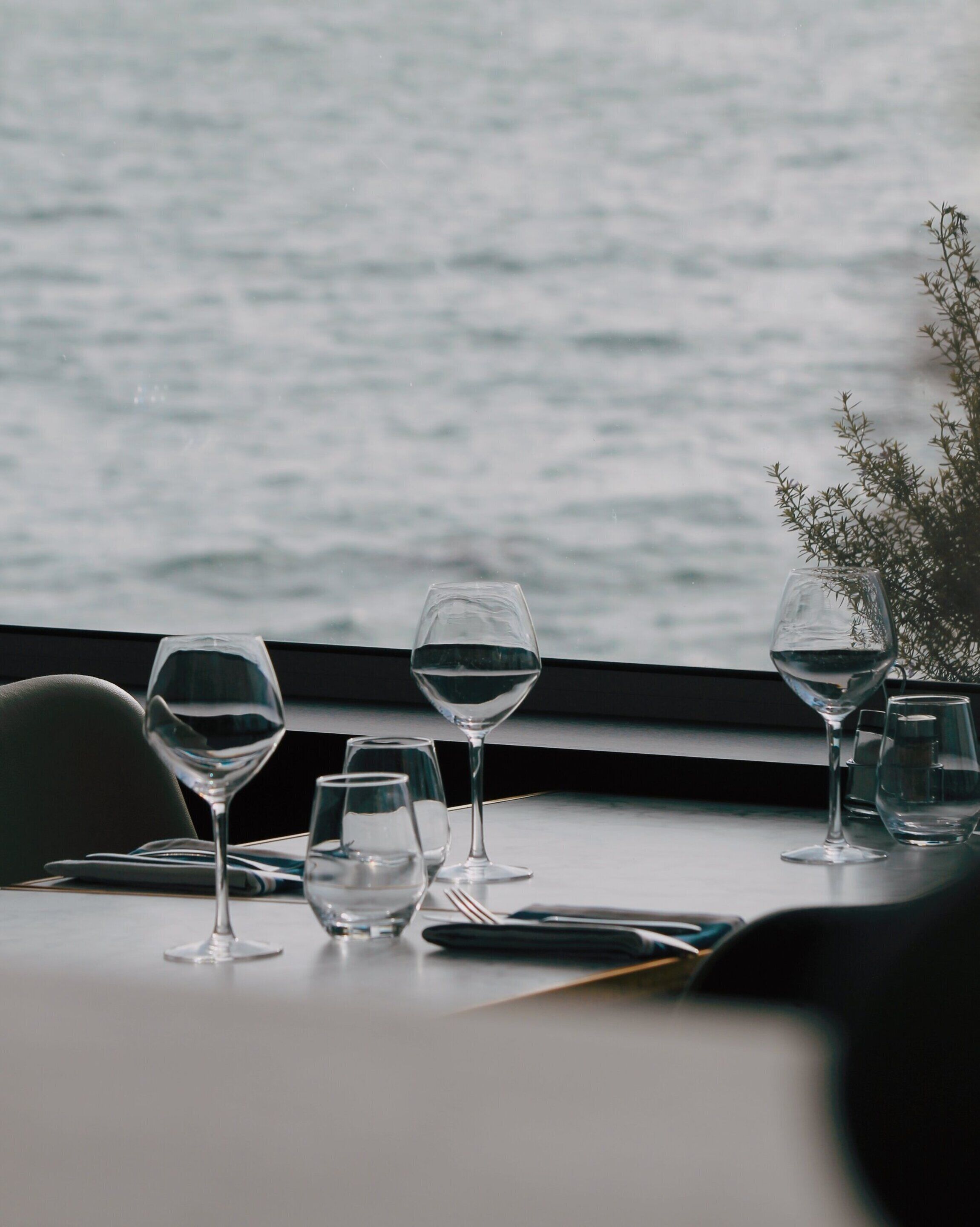 A table set with wine glasses and water glasses, overlooking a body of water.