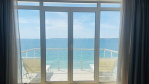 A room with a large sliding glass door leading to a balcony with a view of the sea and a distant shoreline. - Les Sables Blancs (Concarneau)
