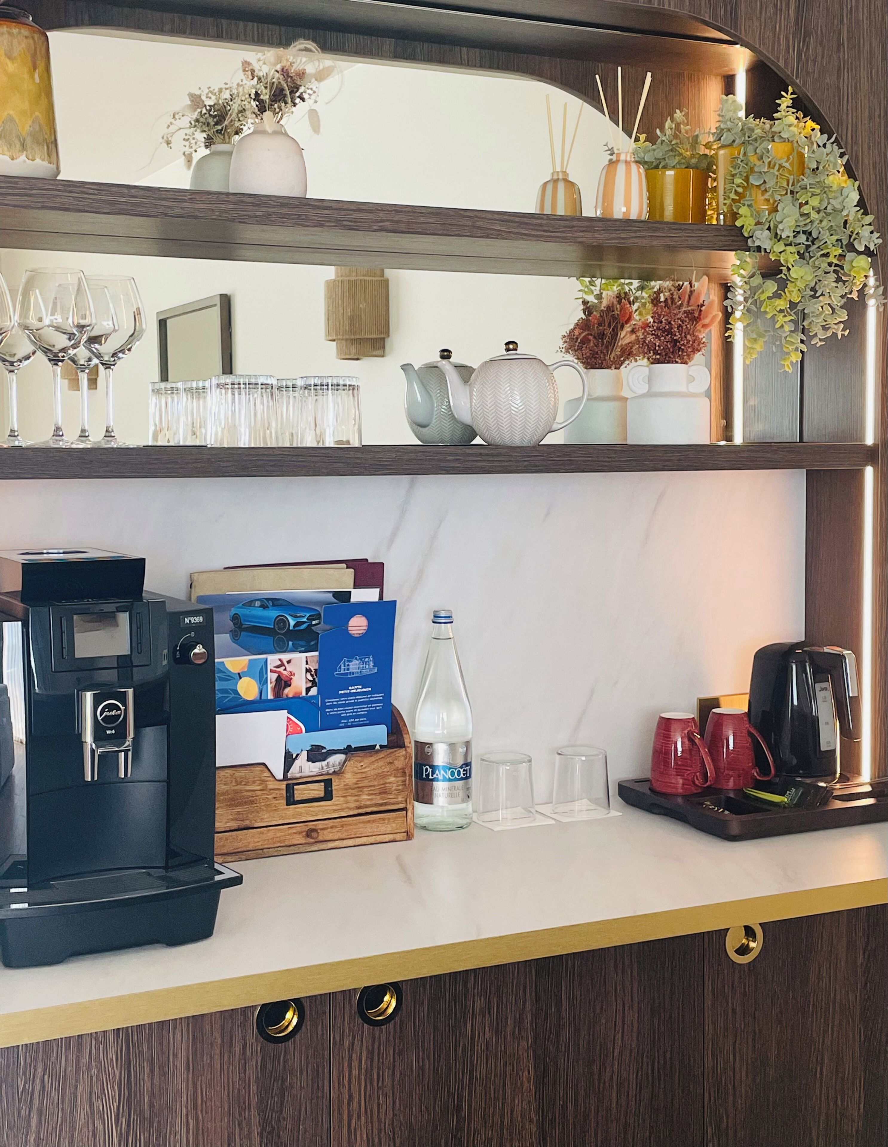 A hotel room's minibar with a coffee maker, a bottle of water, and a tray with red cups.