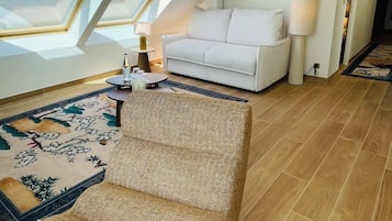 Quarto moderno no estilo loft, com teto inclinado, claraboias, um sofá branco, uma mesinha redonda e um tapete estampado.
