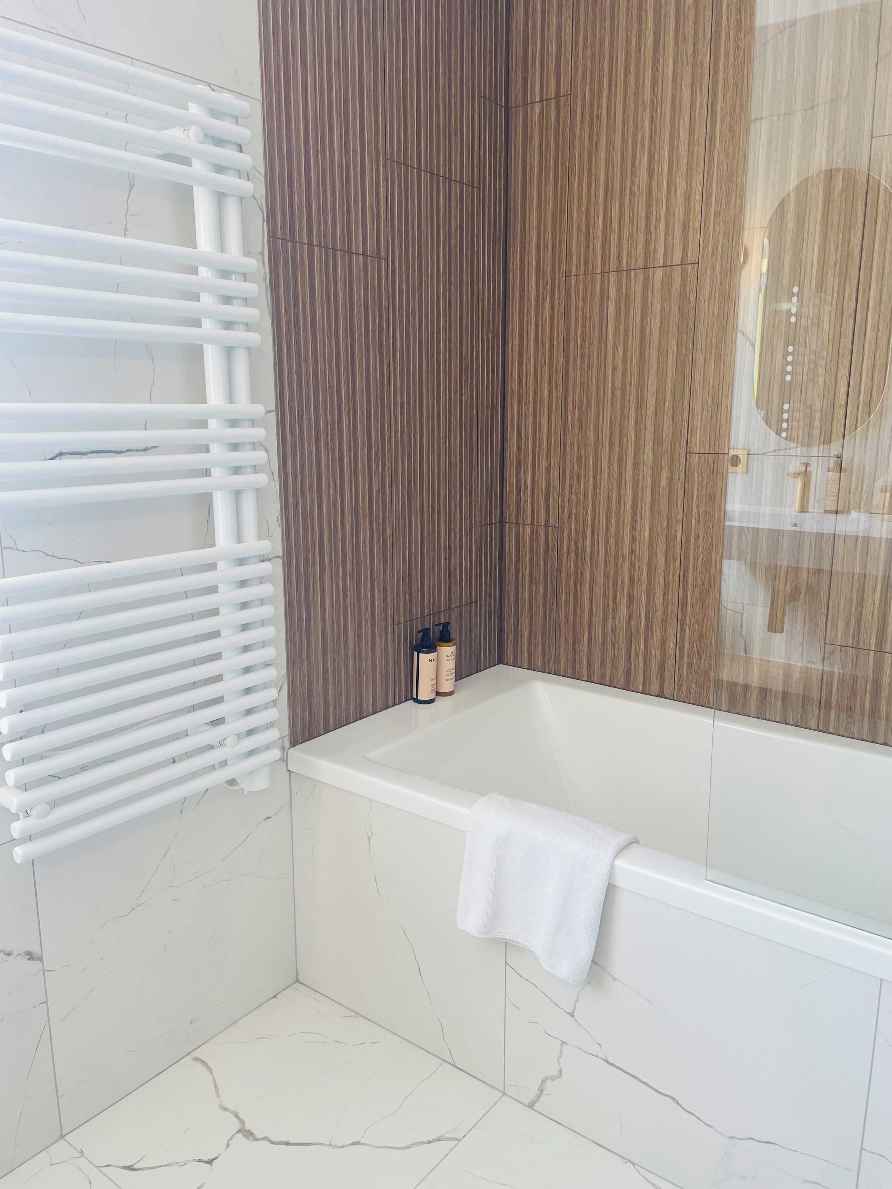 Un baño con bañera, una toalla blanca y una zona de ducha con un perchero blanco.