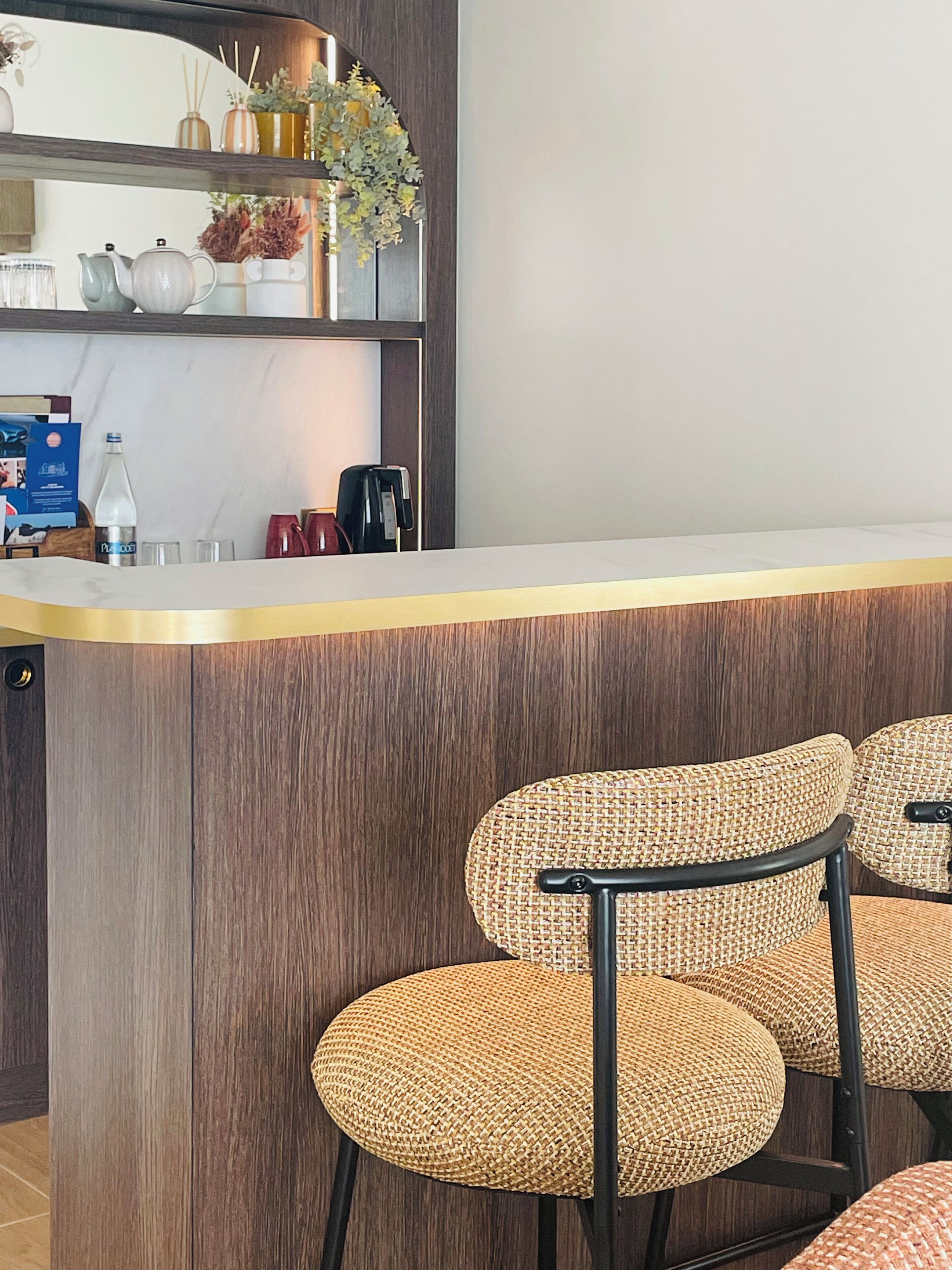 A bar area with a wooden counter, wicker chairs, and a shelf with various items.