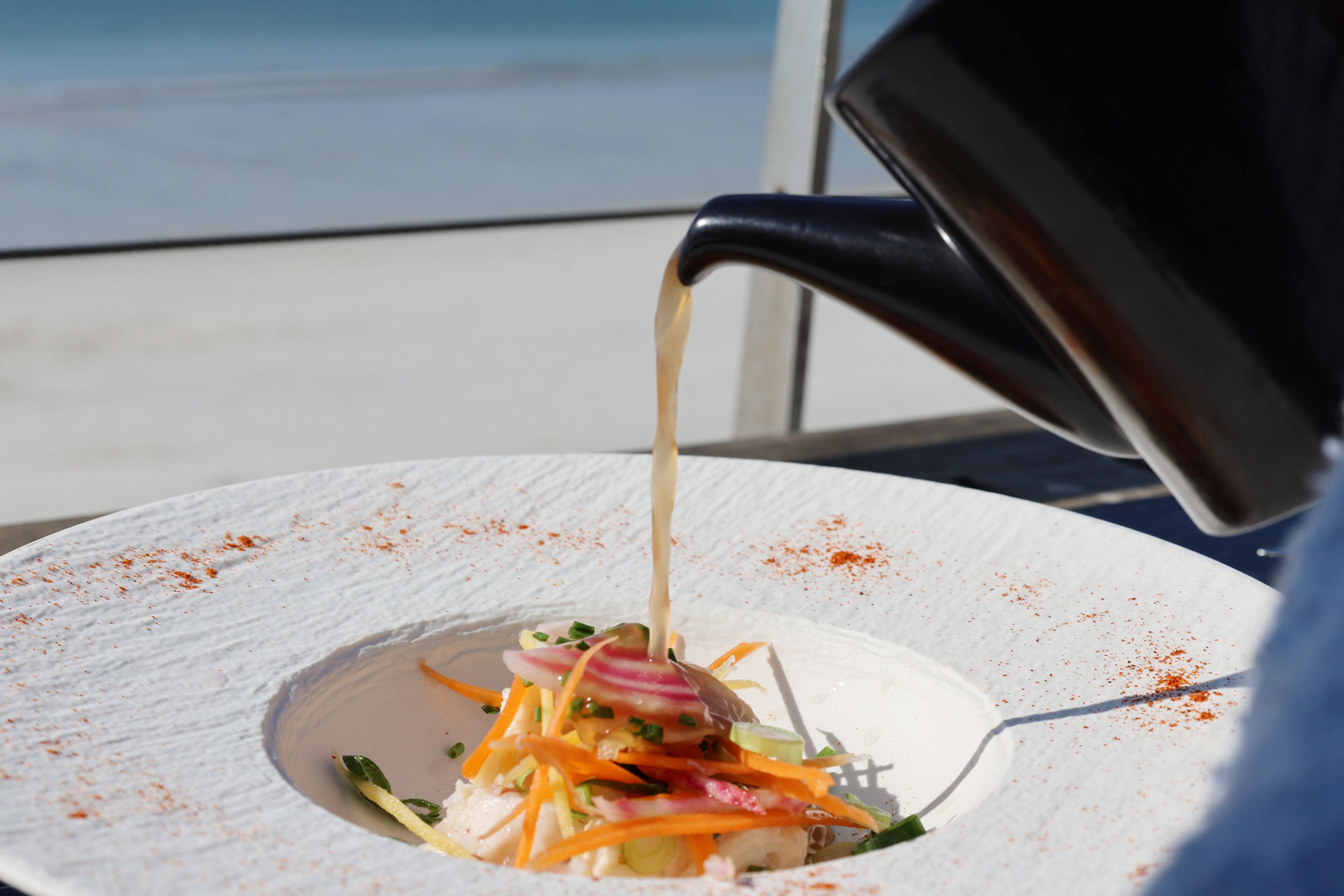 A white plate with a salad and a dressing being poured over it.