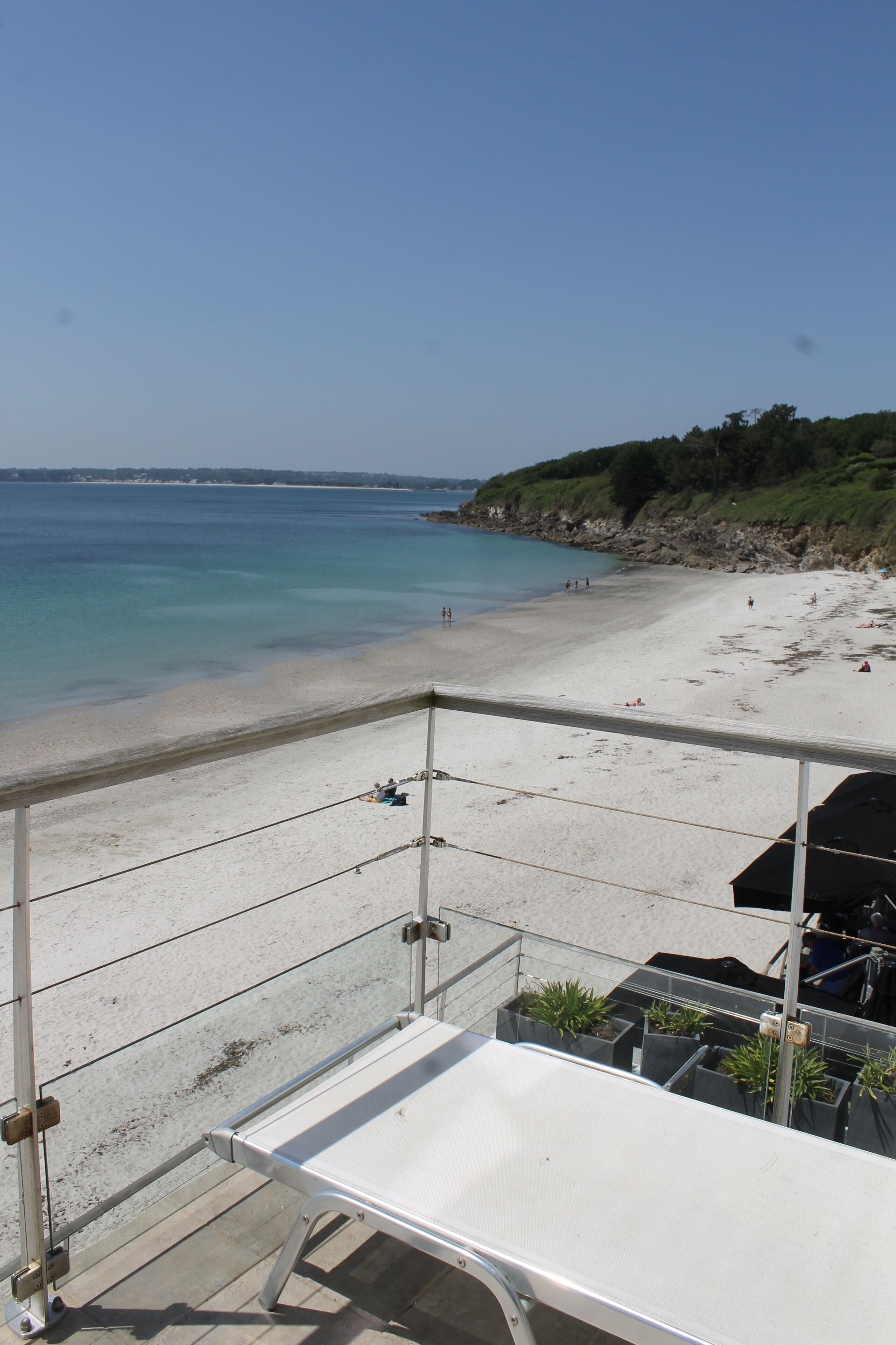 A beach view with a white sandy shore, clear blue water, and a few people in the distance.