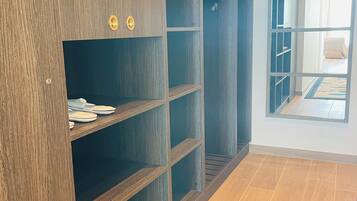 A room with a large wooden wardrobe, a tiled floor, and a view through an open door.