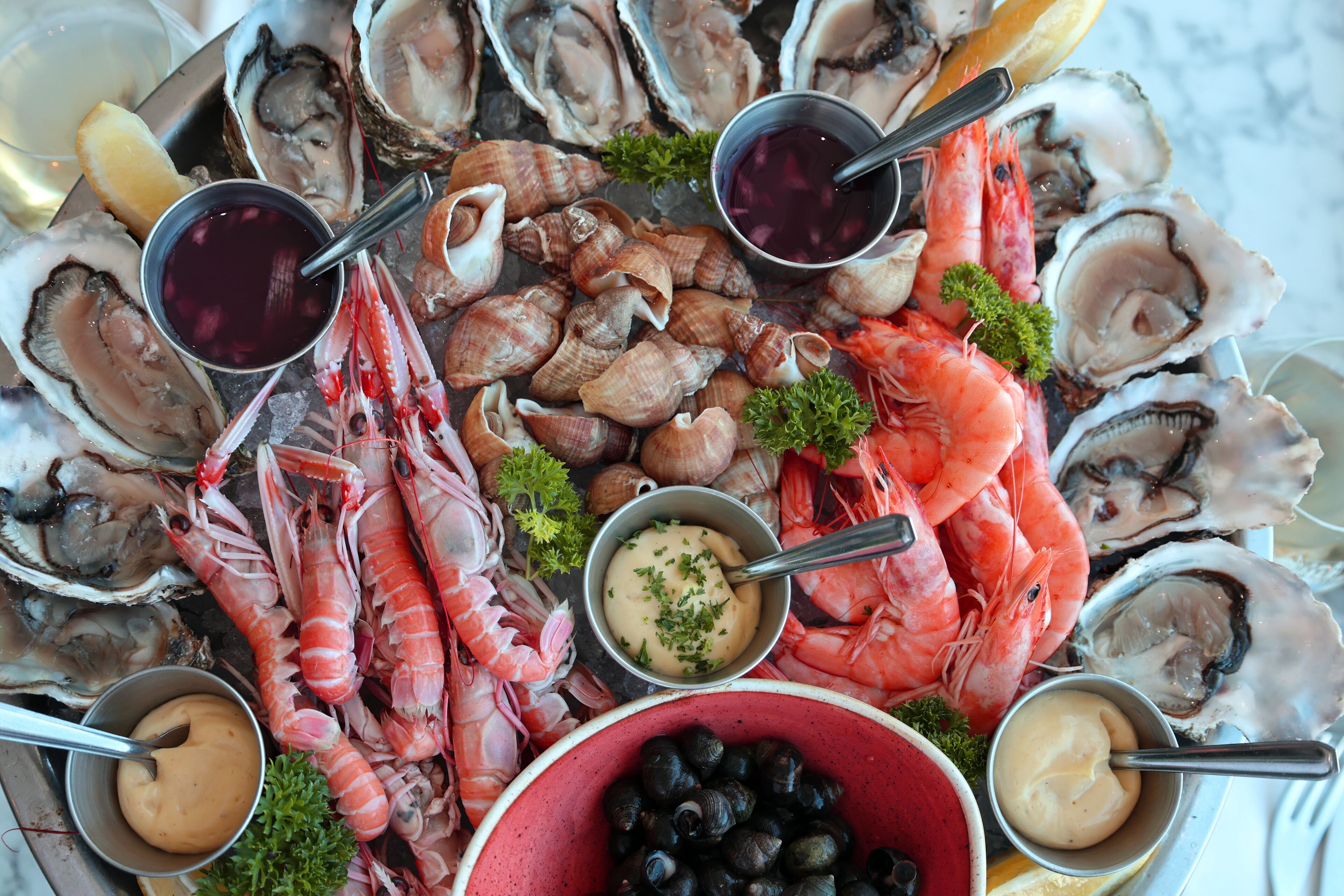 A seafood platter with oysters, shrimp, mussels, and various sauces.