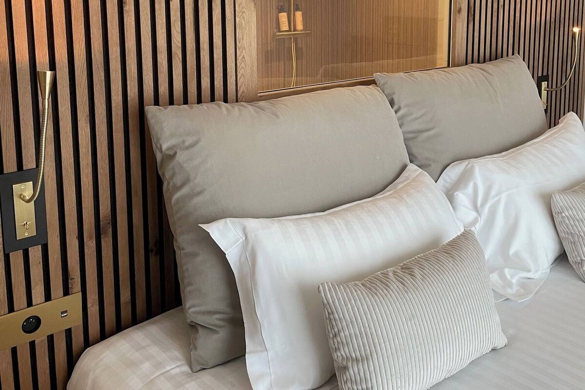 Un dormitorio con pared de listones de madera, un espejo grande y una cama con muchas almohadas.
