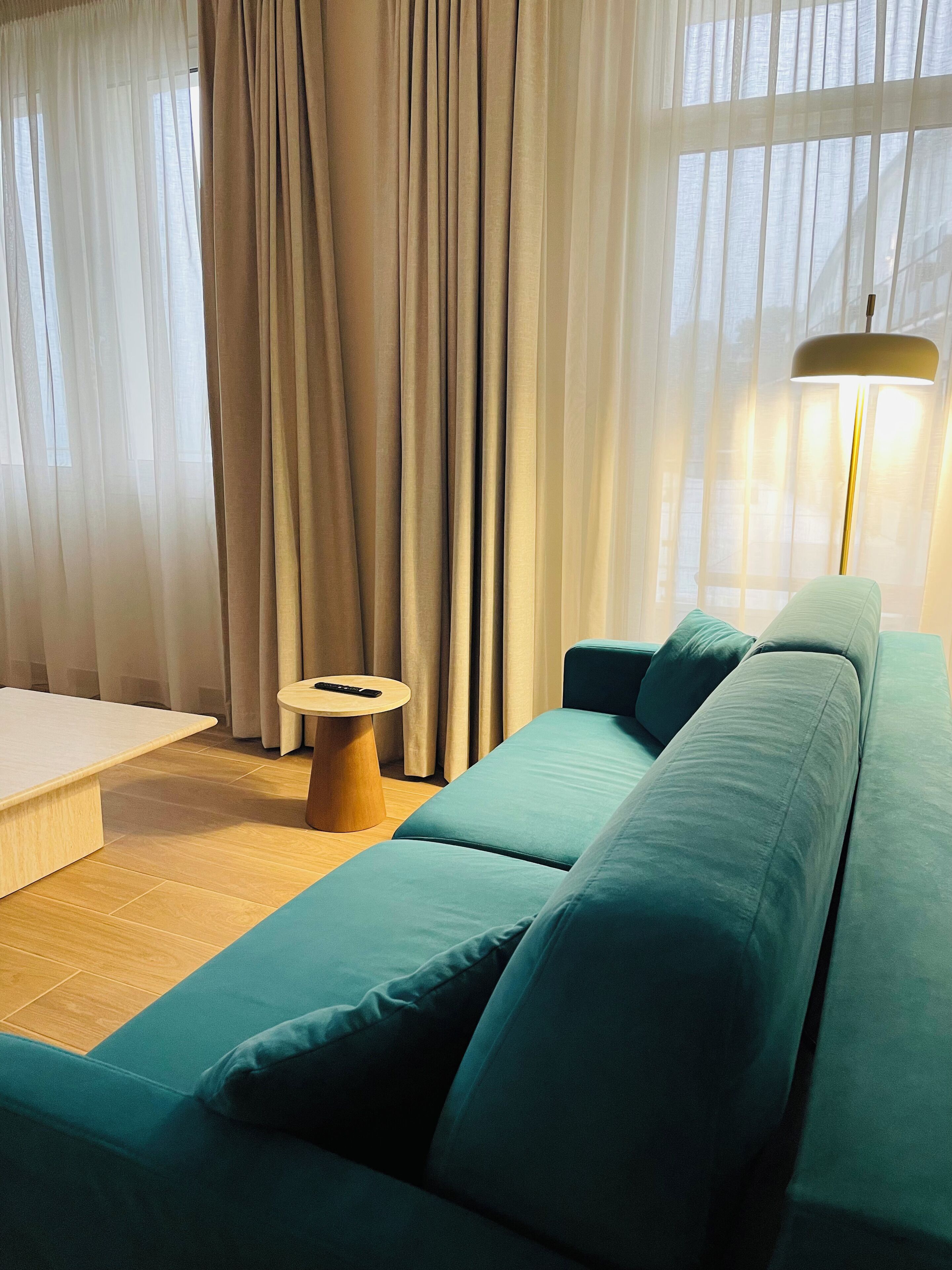 A modern living room with a teal sofa, a small wooden side table, and a remote control on it.