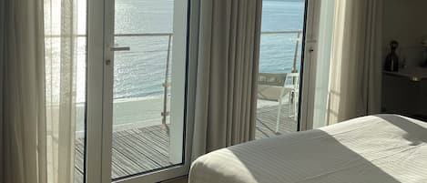 A hotel room with a large bed, a balcony with a view of the sea, and a TV mounted on the wall.