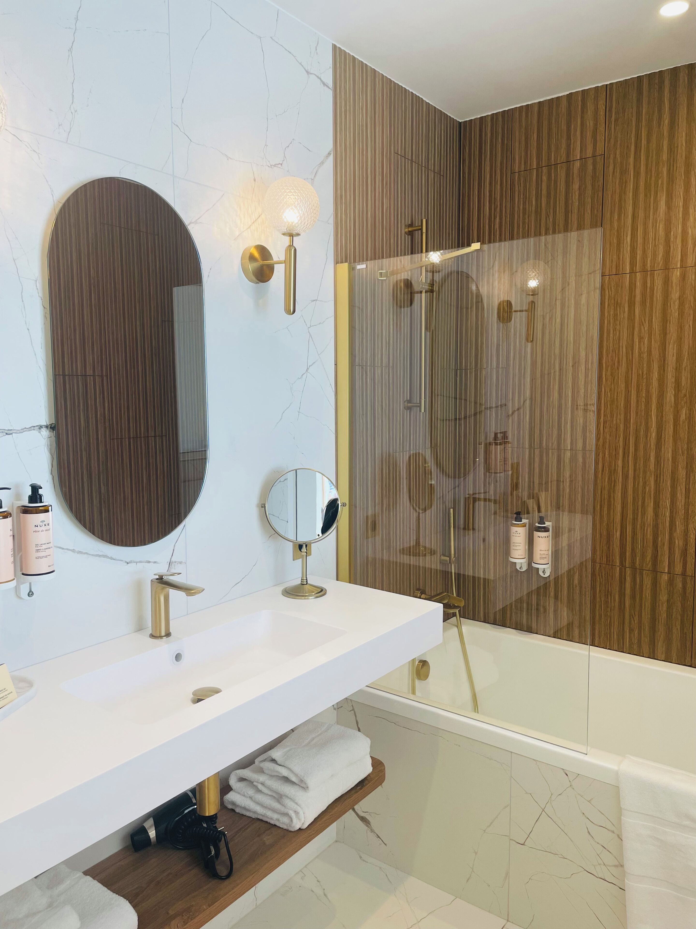 Une salle de bain moderne avec un meuble-lavabo en marbre, un grand miroir, une douche à parois de verre et un lambris en bois sur les murs.