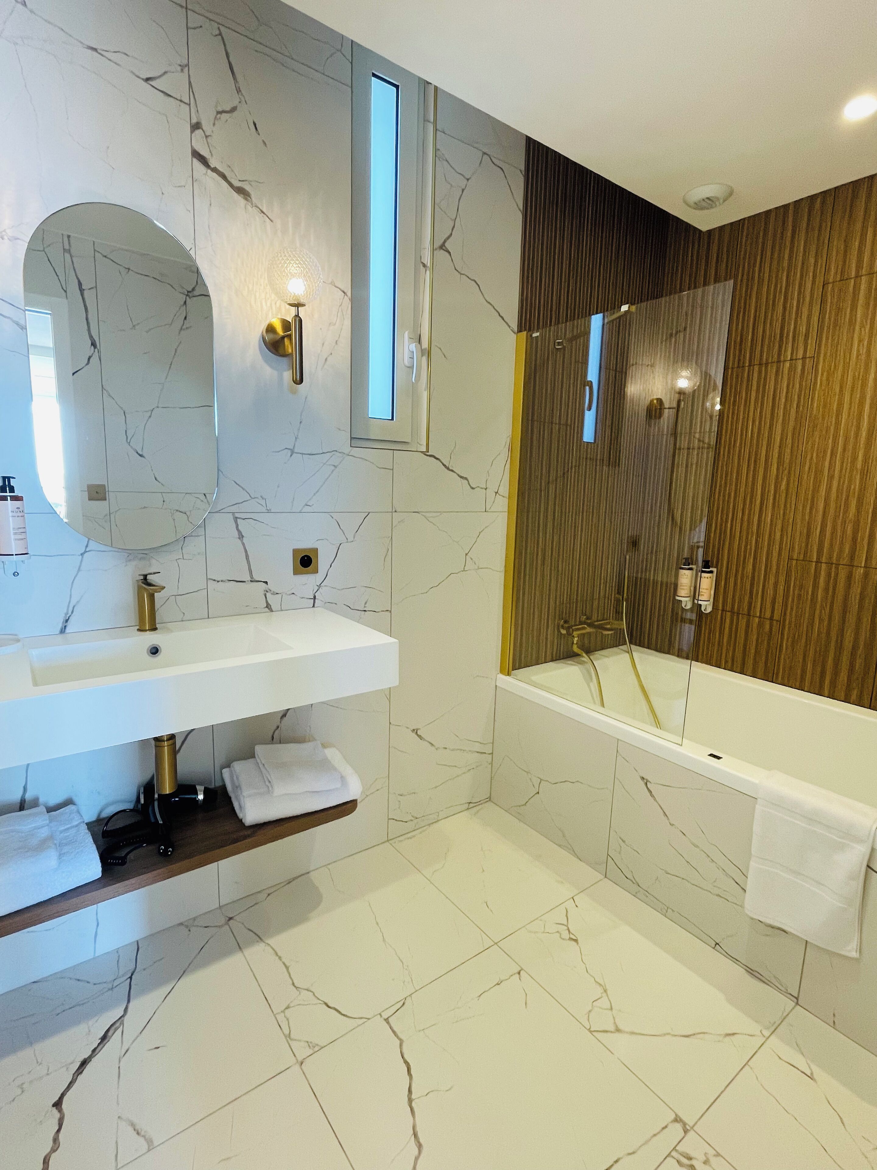 A modern bathroom with a marble backsplash, a white sink, a large mirror, and a bathtub.