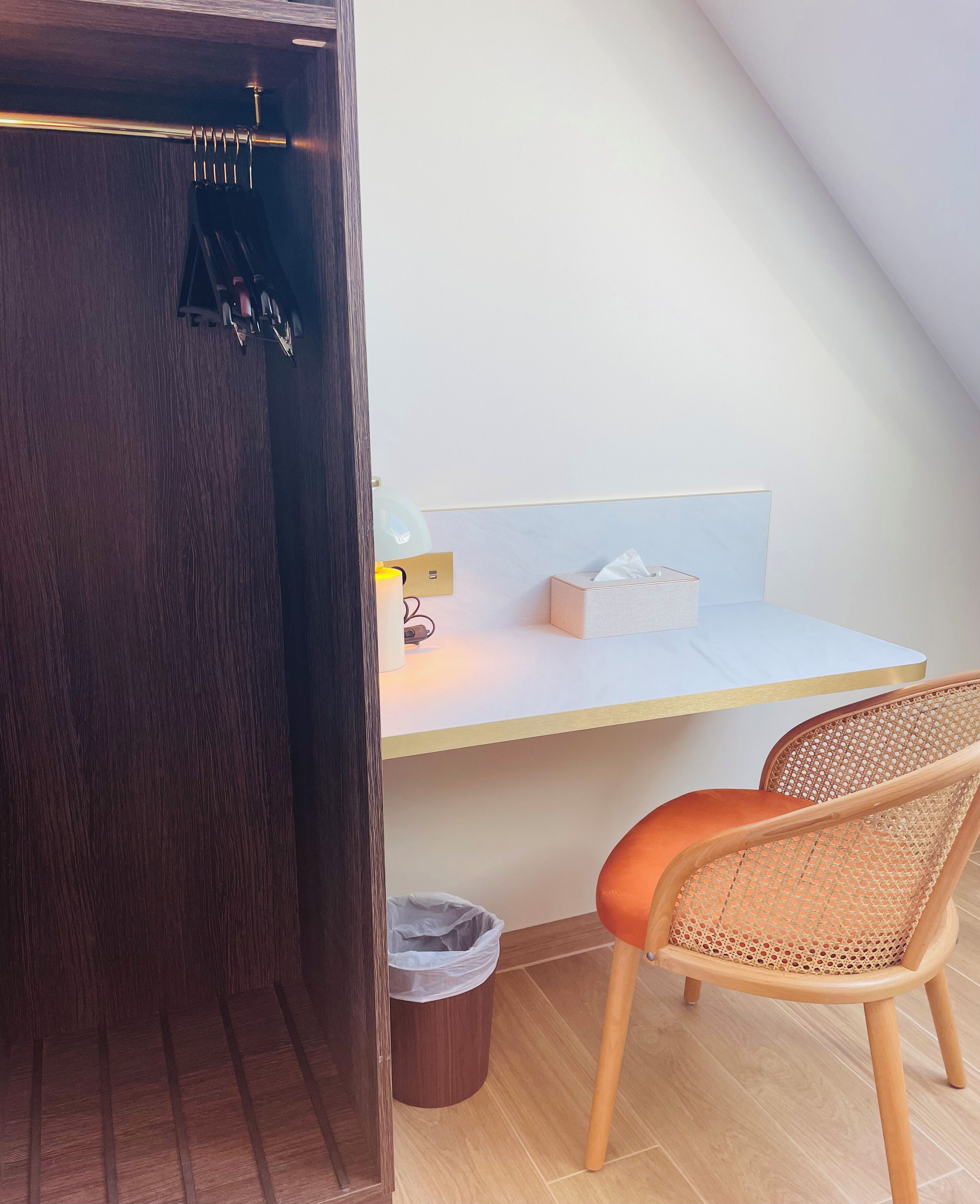 Una habitación con escritorio, silla, cesto de basura y puerta de madera.