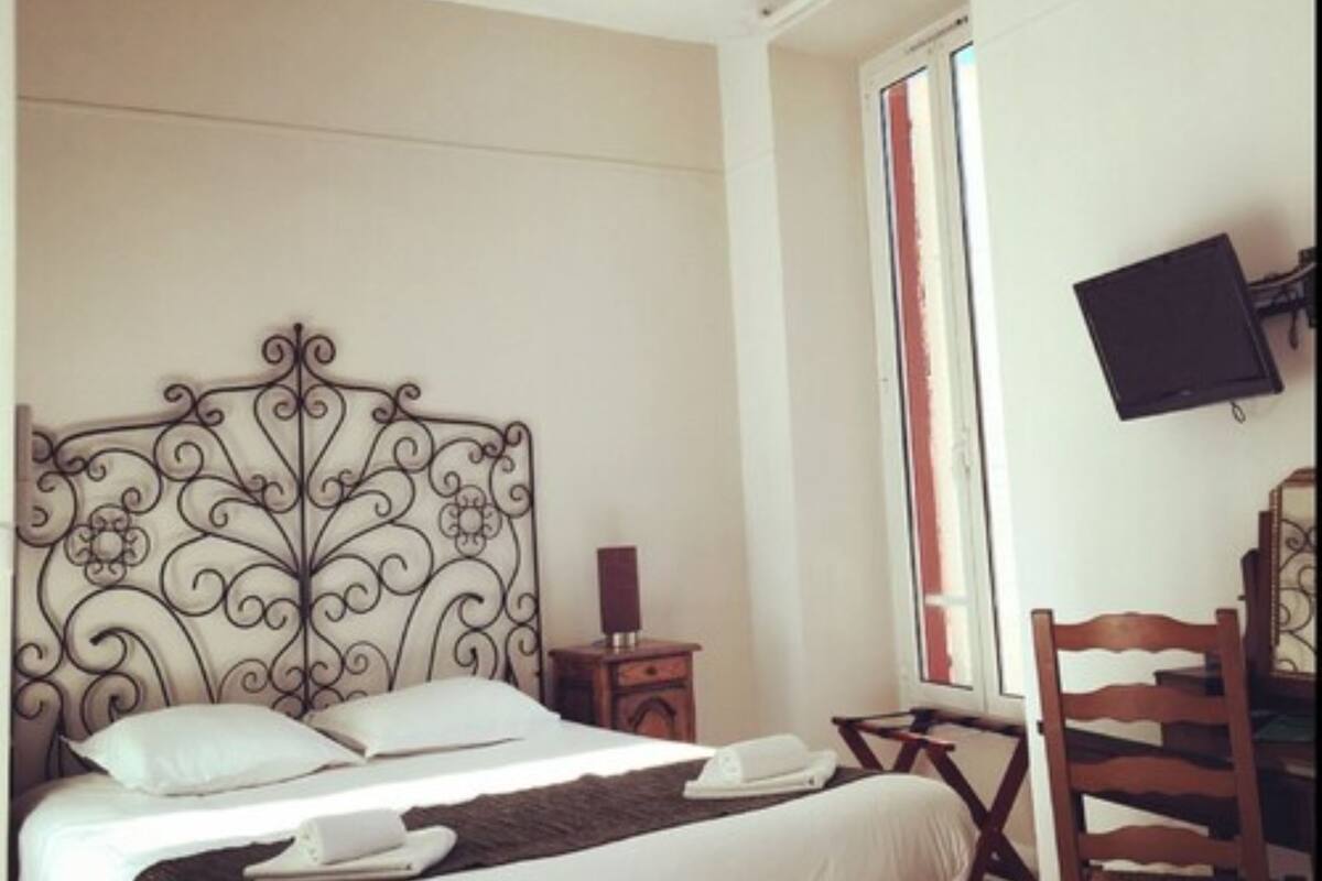 Un lit bien fait, agrémenté d’une tête de lit décorative, une table de chevet avec une lampe, une chaise et un téléviseur fixé au mur.