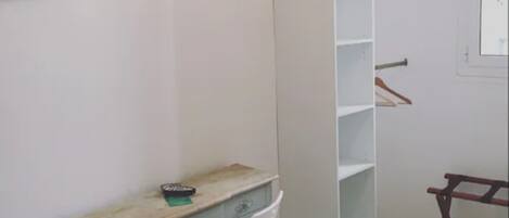 A room with a desk, chair, wardrobe, and a TV mounted on the wall.