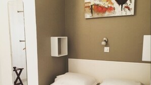 A hotel room with a bed, a wall-mounted mirror, a painting, and a bedside table with a lamp. - Hôtel Danemark (Nice)