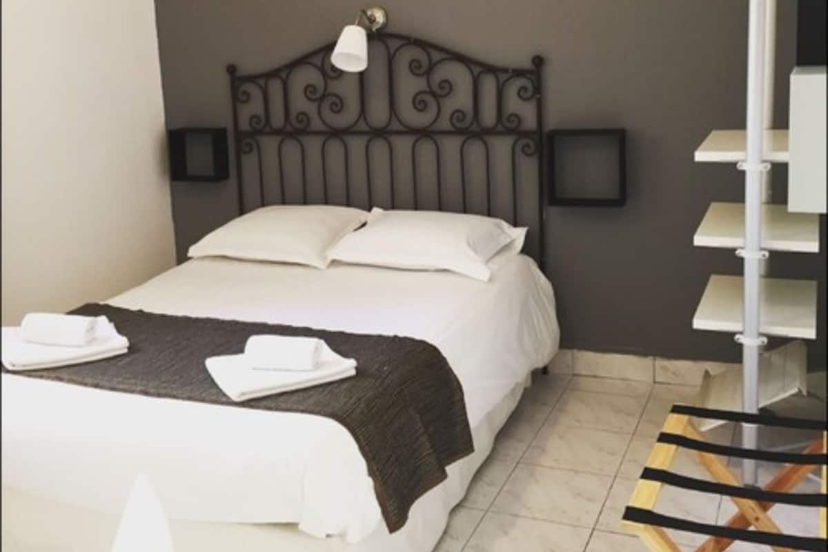 Un lit bien fait, avec du linge de lit blanc, une tête de lit sombre et une lampe de chevet.