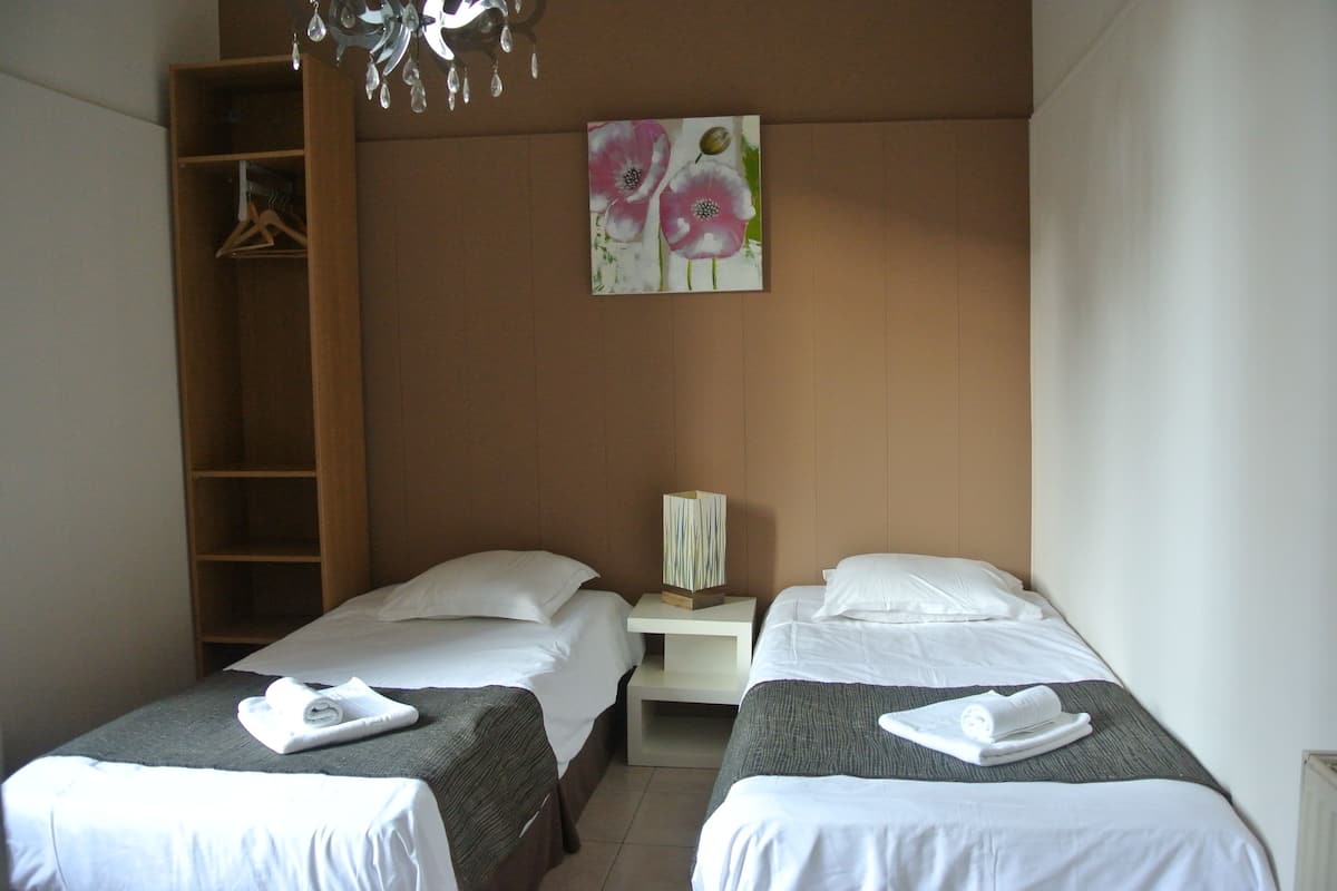 Une chambre d’hôtel avec deux lits, une armoire en bois, un tableau de fleurs et une table de chevet avec une lampe.