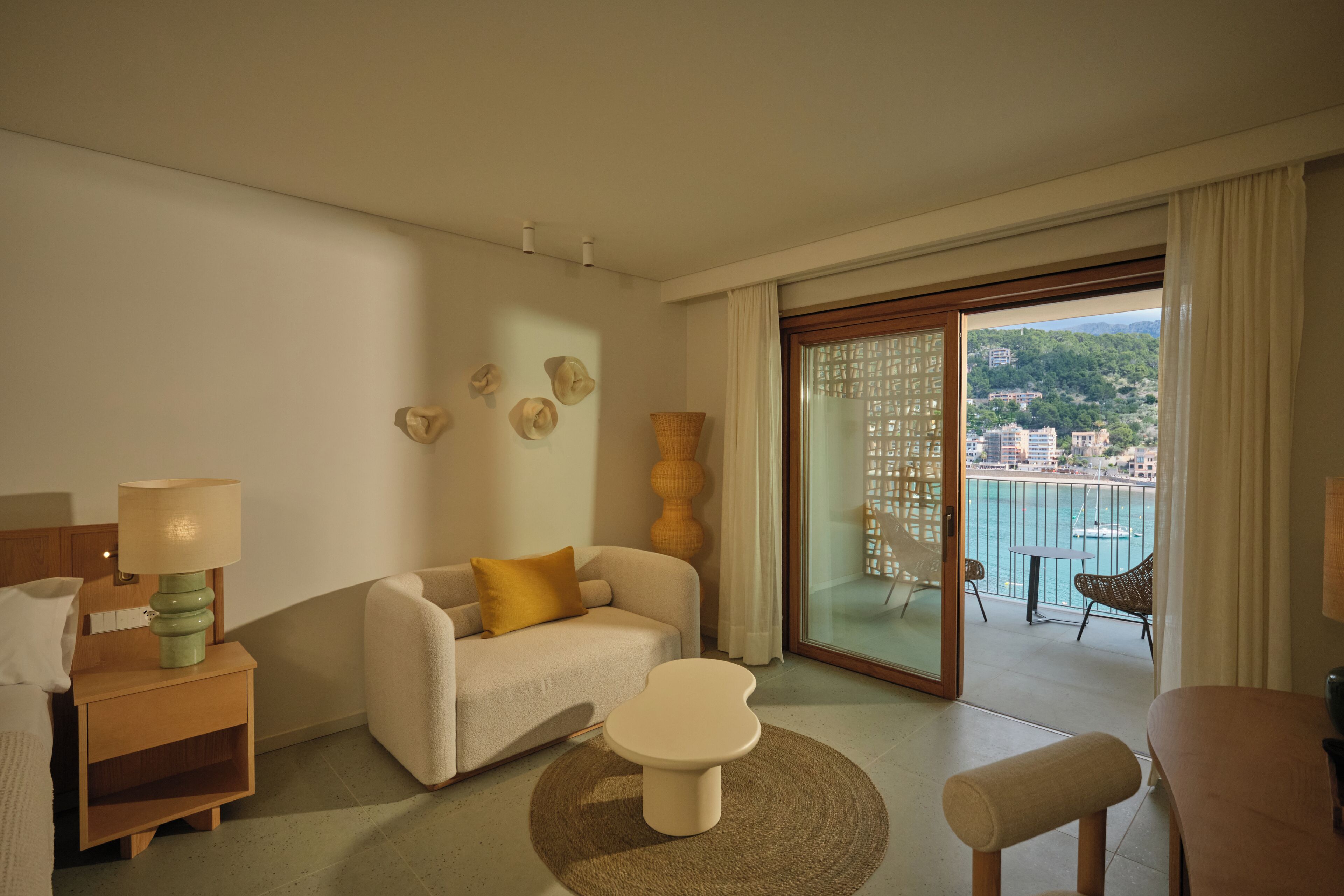 Una habitación de hotel moderna con un sofá, una mesita, una lámpara y vistas al mar a través de un ventanal corredero.