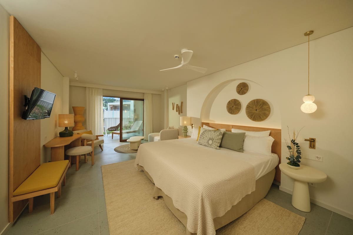 A modern bedroom with a large bed, a desk, and a TV mounted on the wall.