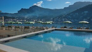 A pool area with multiple green umbrellas, lounge chairs, and a view of a coastal town with mountains in the background. - Hotel Salino Port Soller - Adults Only +16 (Sóller)