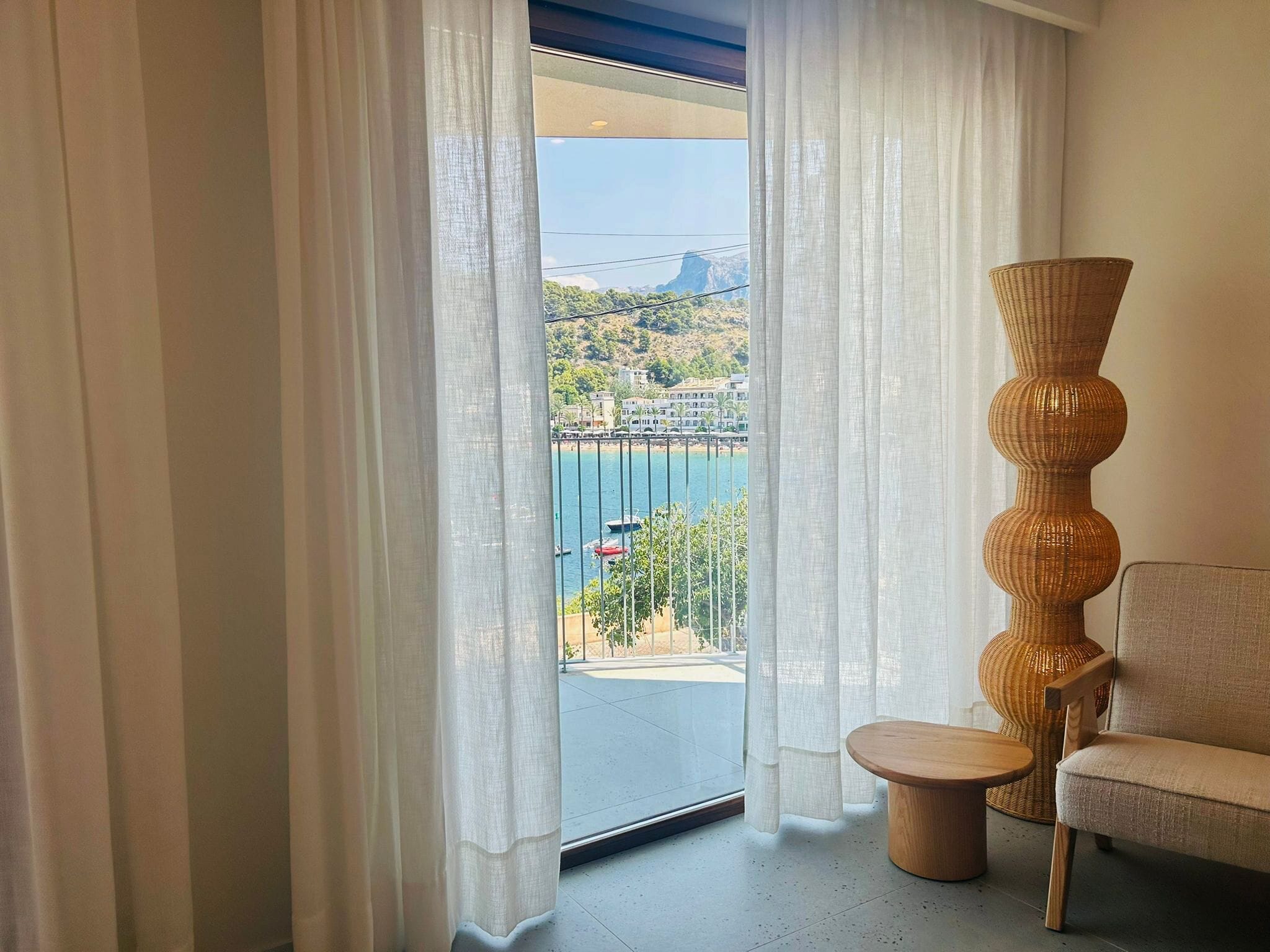 A room with a view of a coastal area, featuring a wicker chair and a small table.