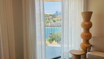 A room with a view of a coastal area, featuring a wicker chair and a small table.
