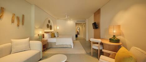 A modern hotel room with a sofa, a small table, a bed, and a desk area.