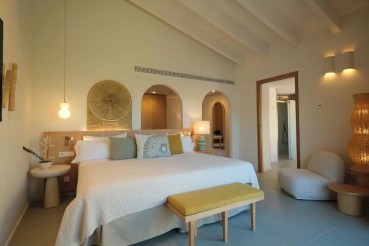 A modern hotel room with a large bed, bedside tables, a bench, and a mirror.