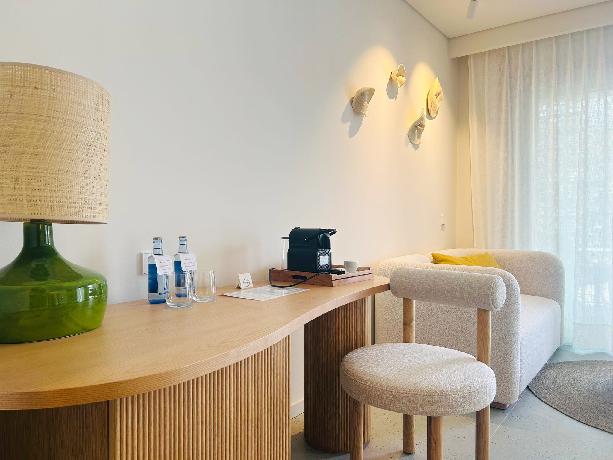 Une chambre d’hôtel moderne avec un bureau en bois, une lampe verte, une machine à café et un fauteuil confortable.