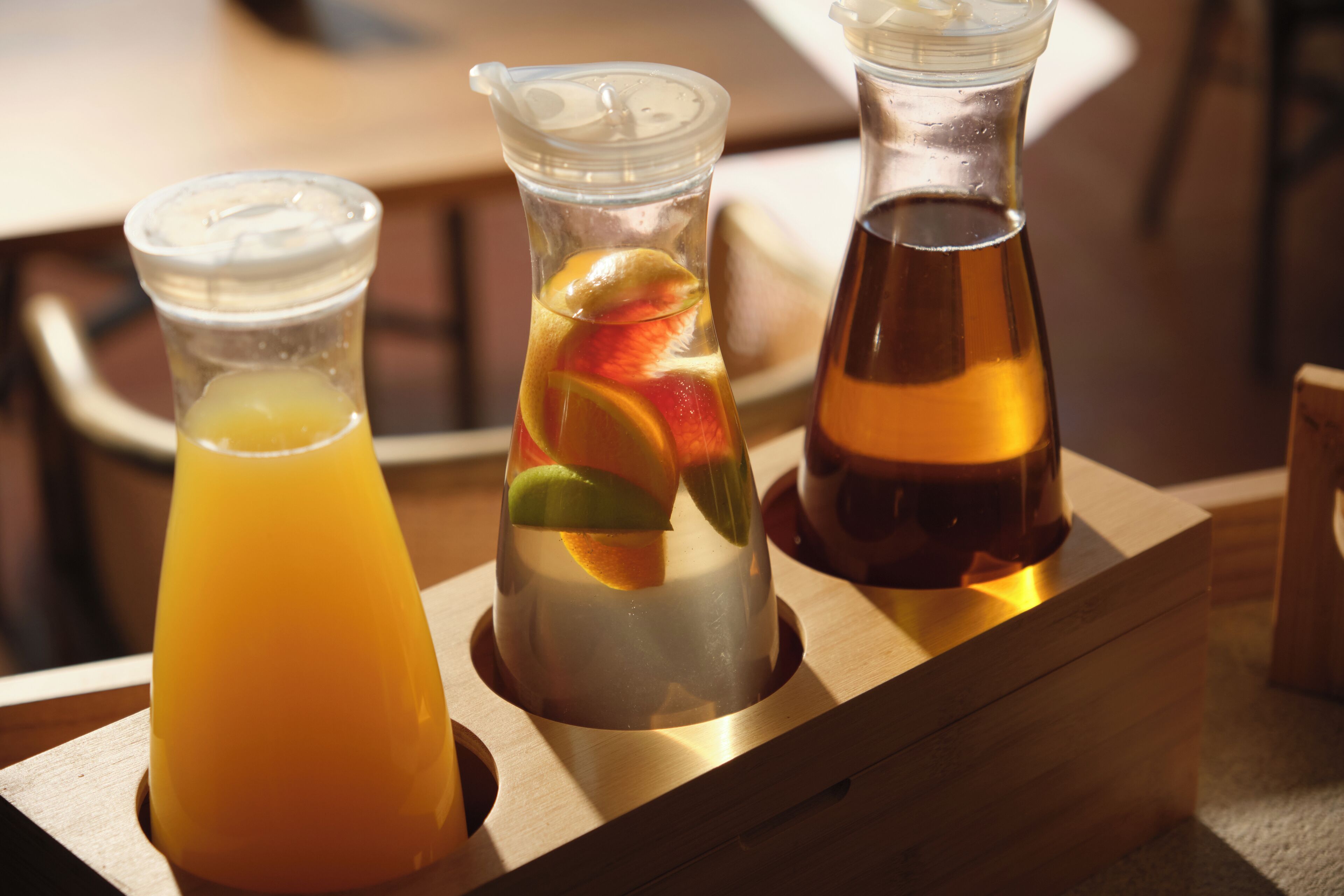 Drie glazen potten met verschillende dranken op een houten dienblad.
