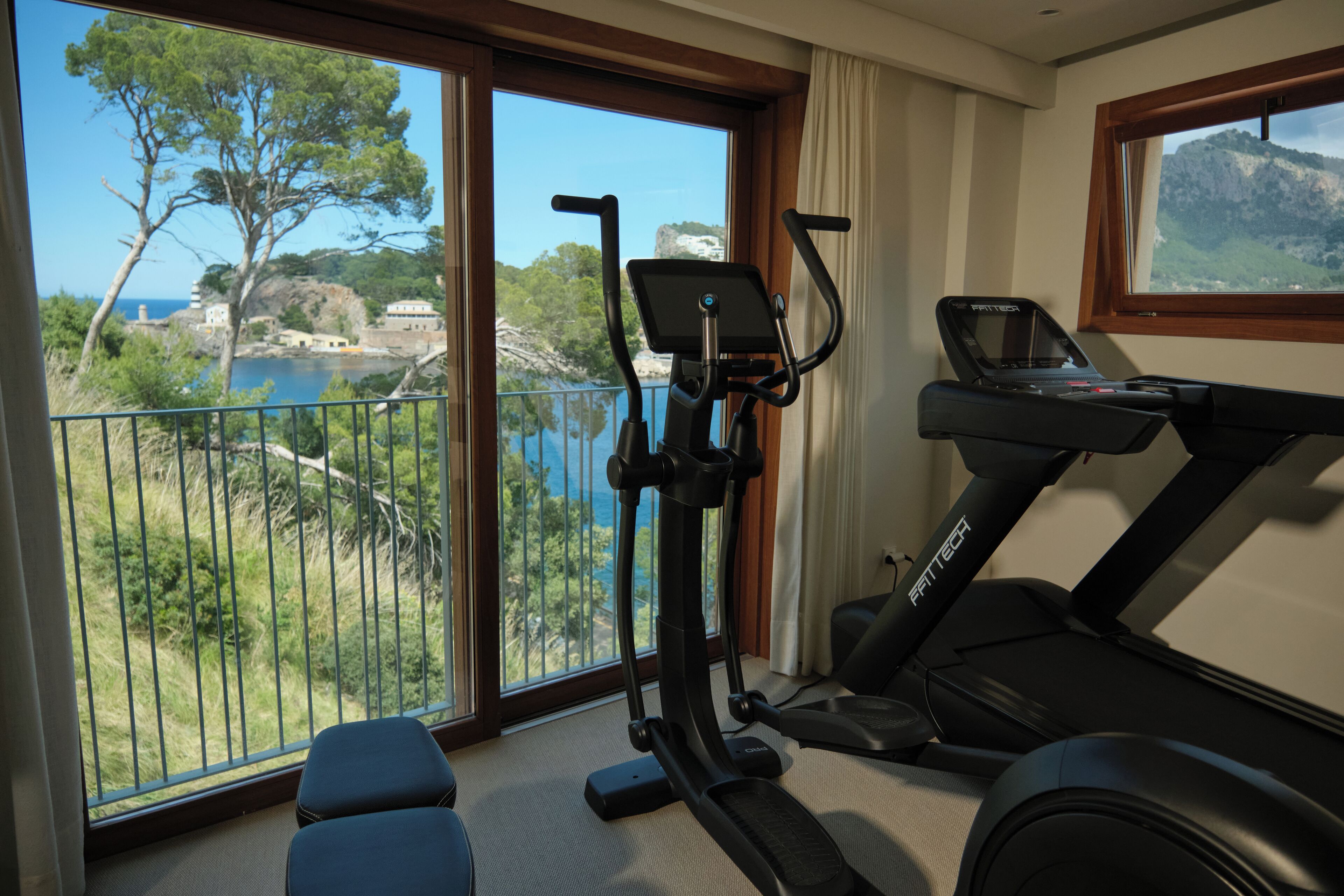 Habitación con vistas a un paisaje costero, que incluye árboles y un cuerpo de agua. Cuenta con una bicicleta estática y una caminadora.