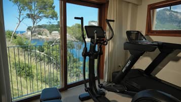 Habitación con vistas a un paisaje costero, que incluye árboles y un cuerpo de agua. Cuenta con una bicicleta estática y una caminadora.