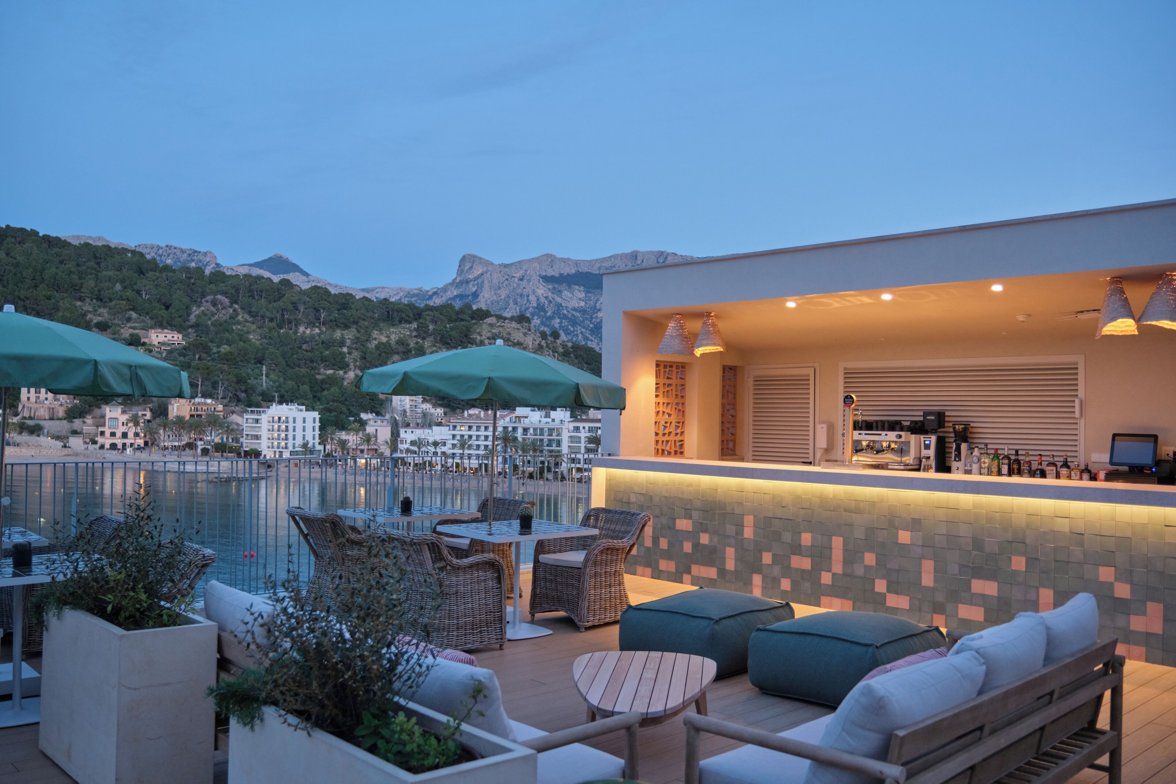 A rooftop bar with outdoor seating, overlooking a body of water and mountains.