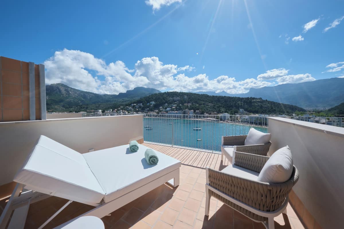 A rooftop terrace with a pool, white lounge chairs, and a view of a mountainous landscape.