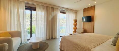A modern hotel room with a large bed, a sofa, a small table, and a TV mounted on the wall.