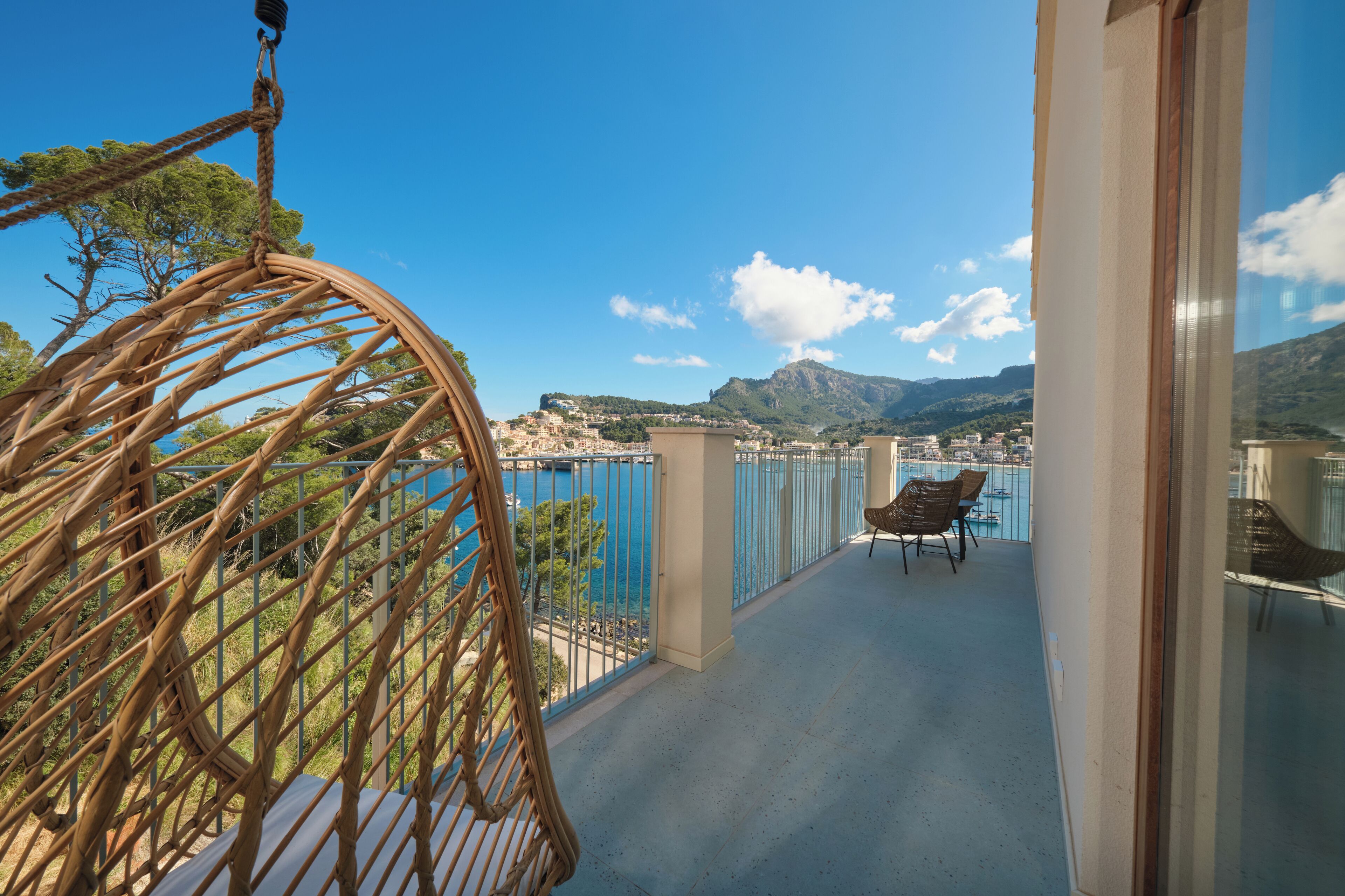 Un balcon avec un fauteuil en osier, une vue sur la mer et une montagne en arrière-plan.
