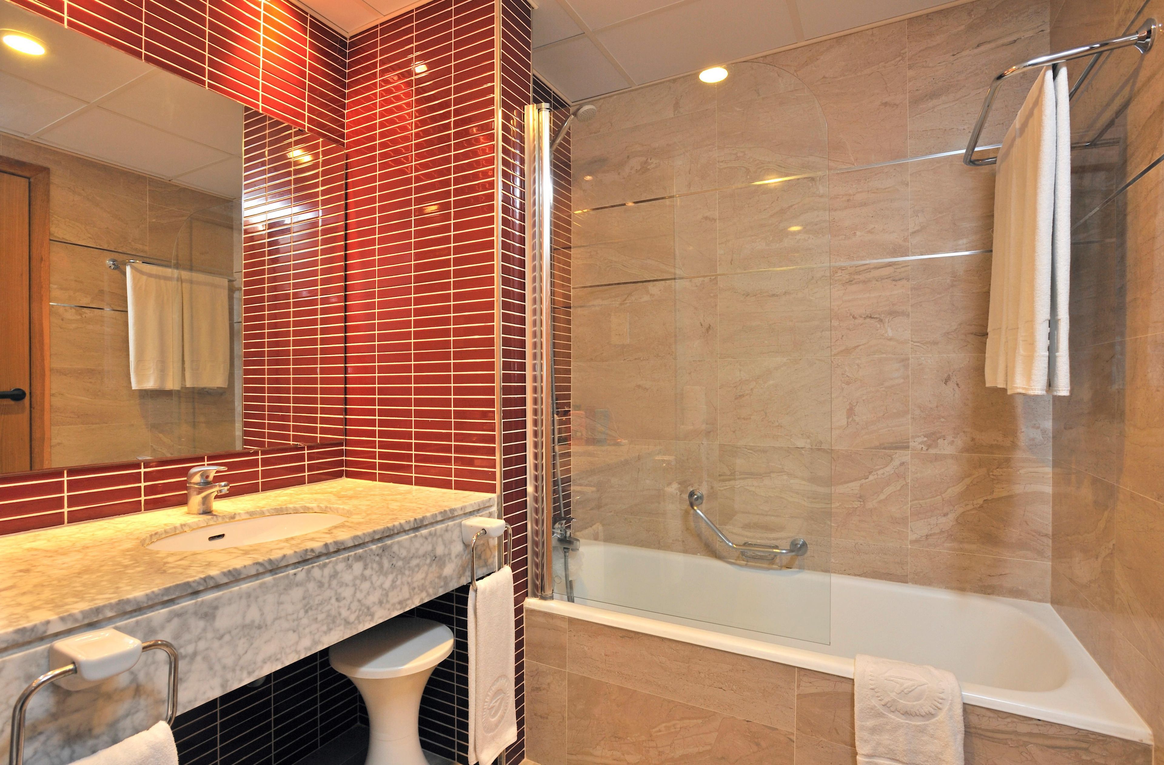 Une salle de bain avec un lavabo en marbre, une douche en verre et un miroir avec un pare-splash en carreaux rouges.