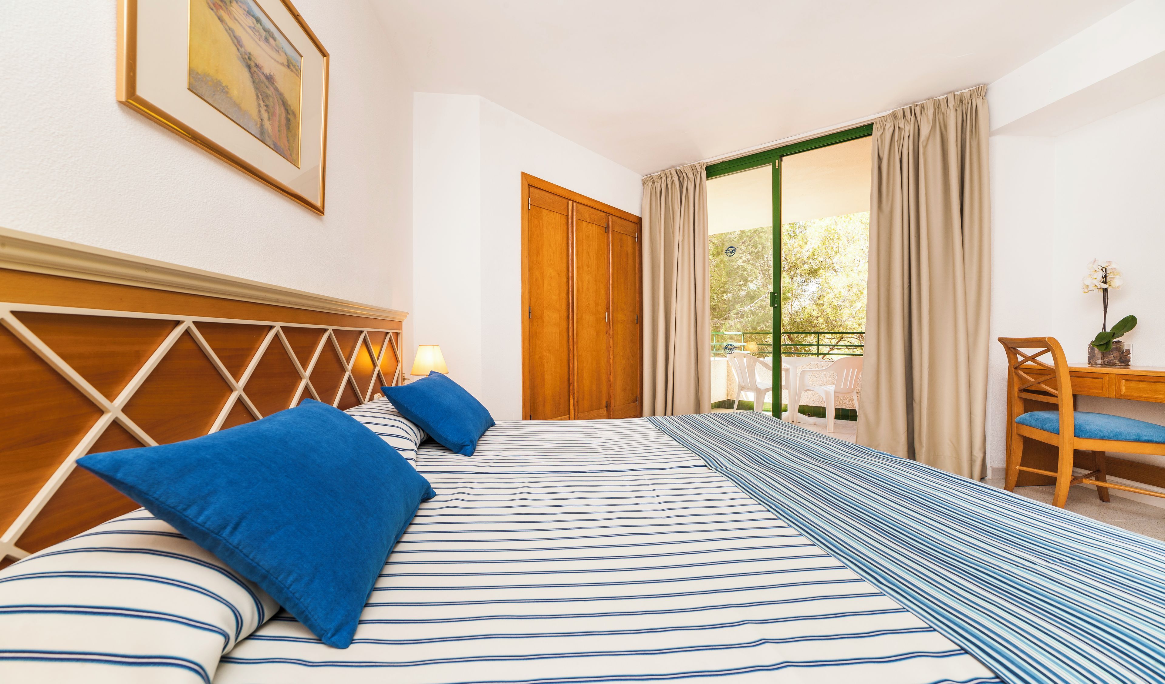 Habitación de hotel con cama, cabecero de madera, escritorio y silla, y vista al exterior.