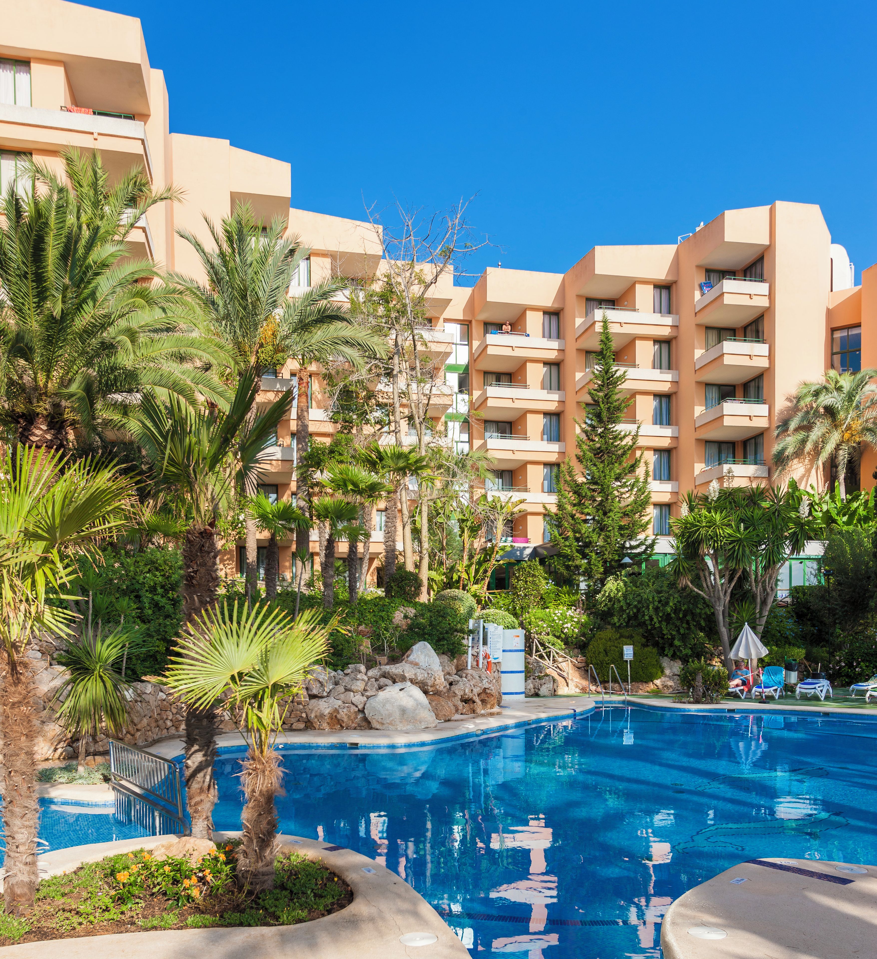 Un hotel con piscina, circondato da palme e vegetazione.