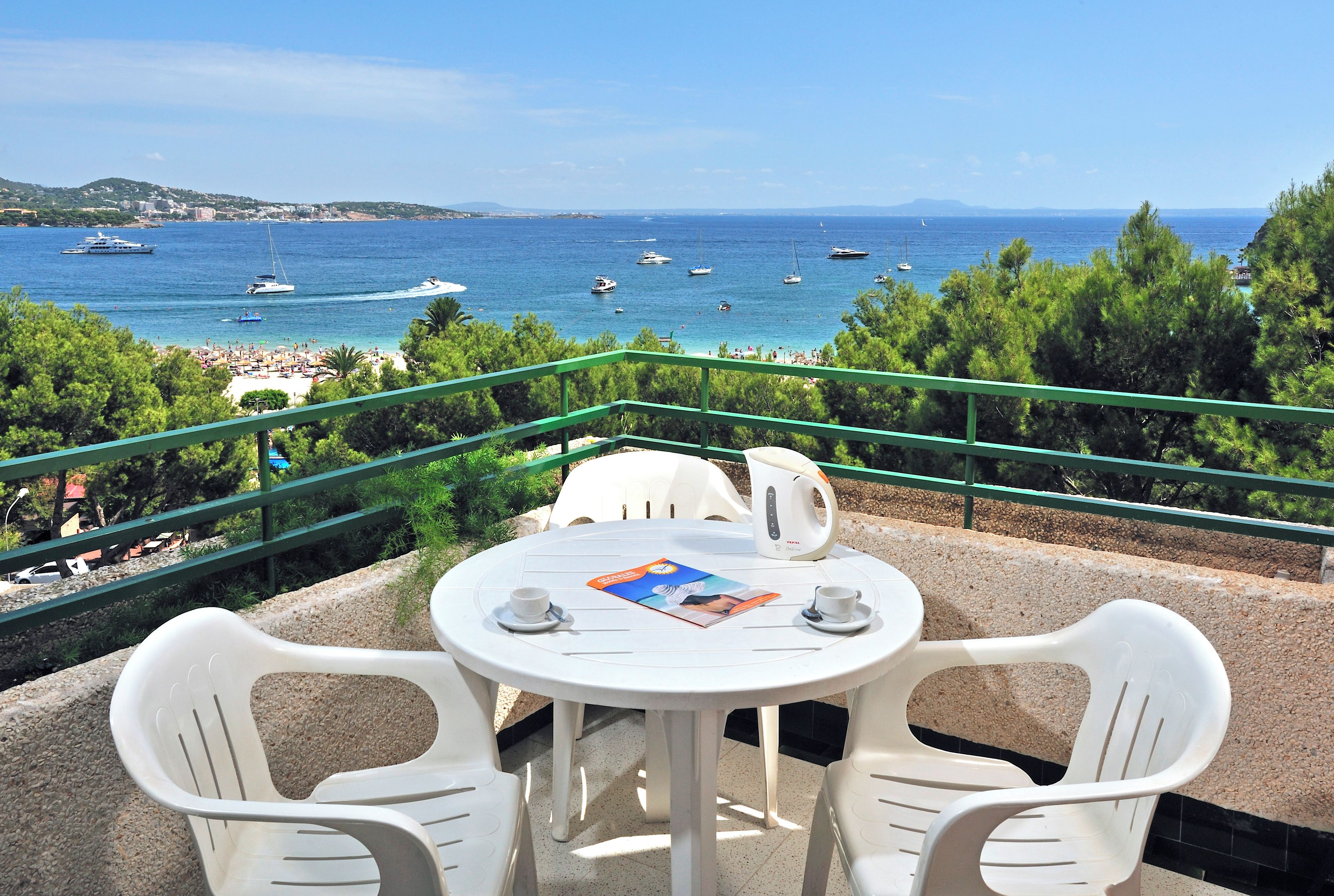 A terrace with a table and chairs overlooking a beach with boats and a clear sky.