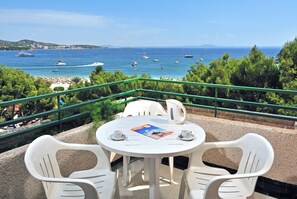 A terrace with a table and chairs overlooking a beach with boats and a clear sky. - Globales Nova (Calvia)